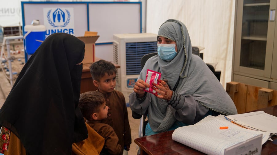 An Afghan family receive a health consultation from a medical staff member wearing a face mask.