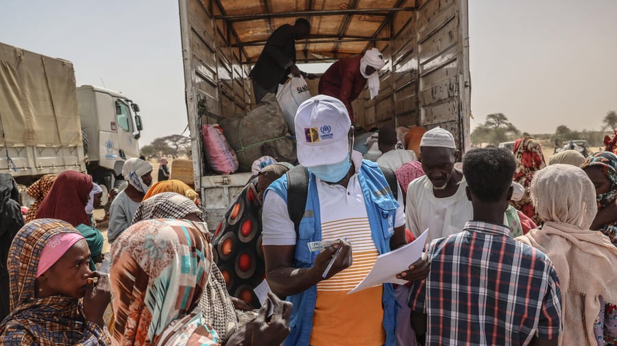 A UNHCR staff member checks documents in a group of people standing at the back of an open truck.