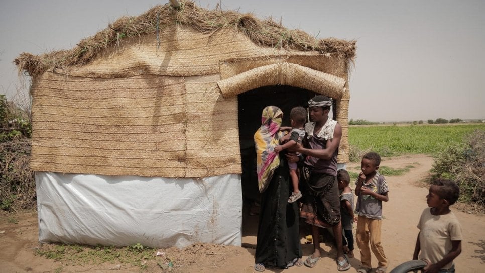 An internally displaced family stand outside a shelter provided by Jeel Albena at a hosting site in Hudaydah, Yemen. © UNHCR/Abdulhakeem Obadi