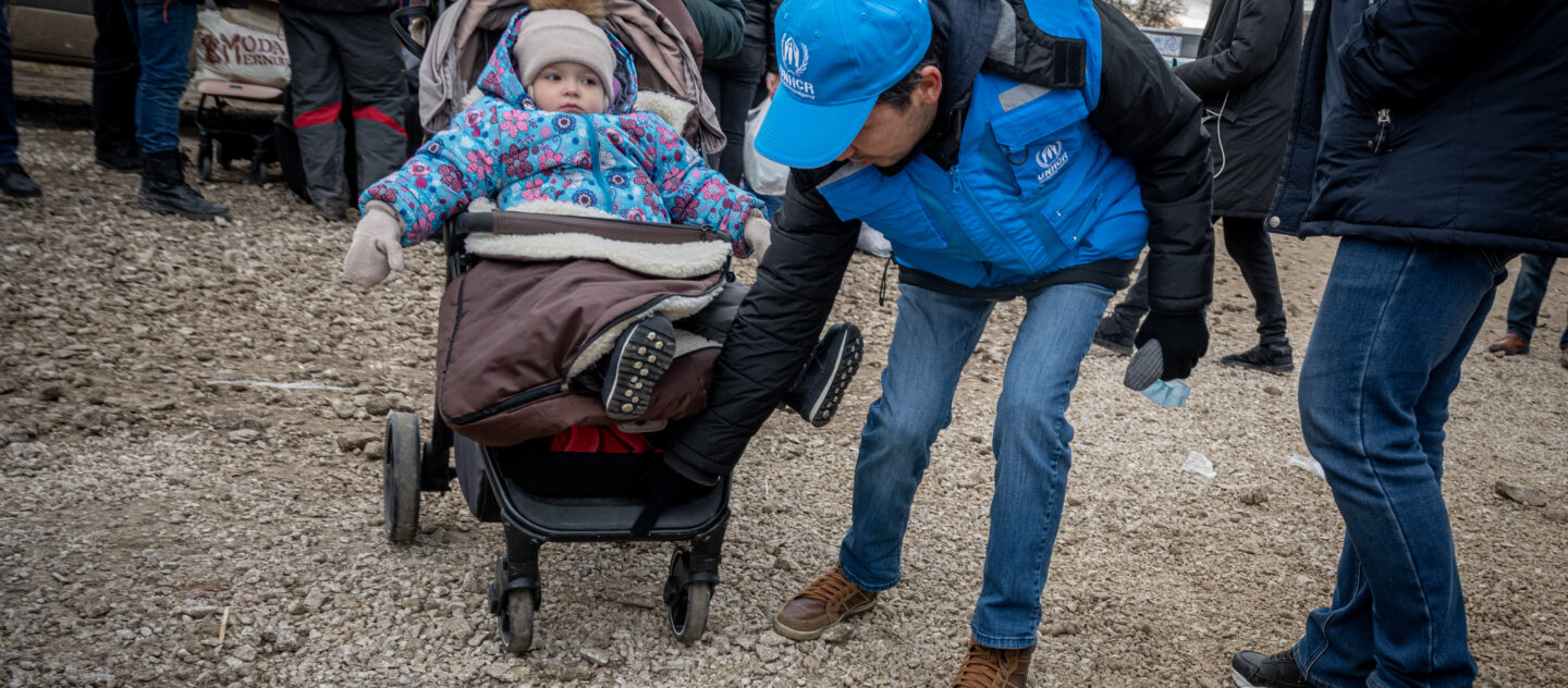 'UNHCR protection officer Batyr Sapbyiev helps a mother and child towards the waiting buses at Moldova’s Palanca border crossing. © UNHCR/Mihai Eremia