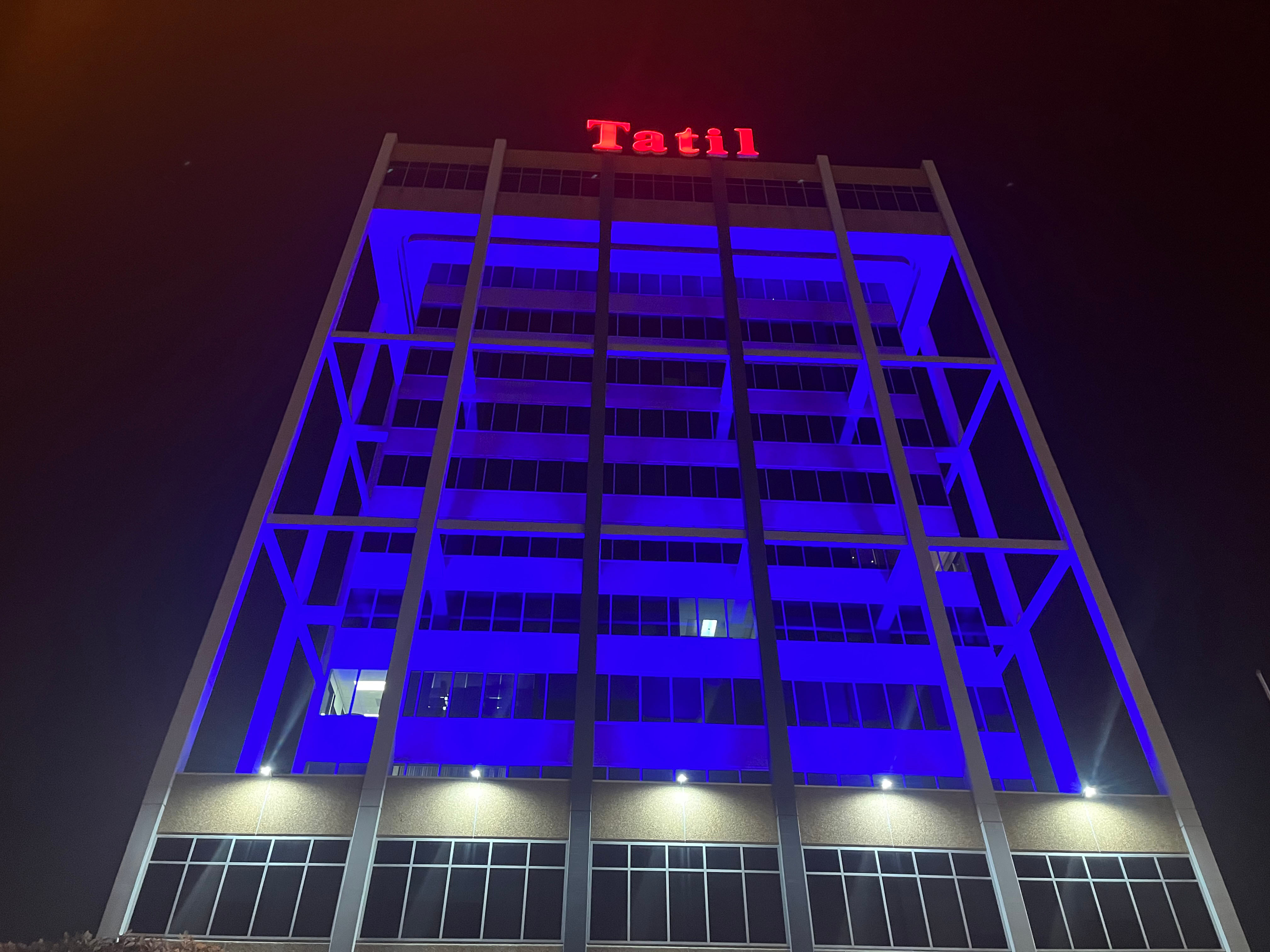 The exterior of a building lit in blue tooped with a red neon sign reading &quot;Tatil&quot;