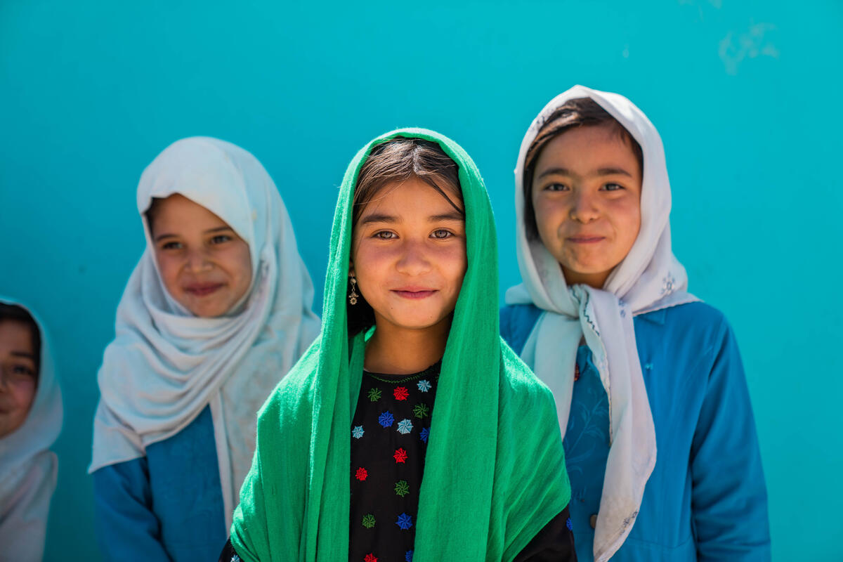 Three girls in colorful headscarves smile for the camera.