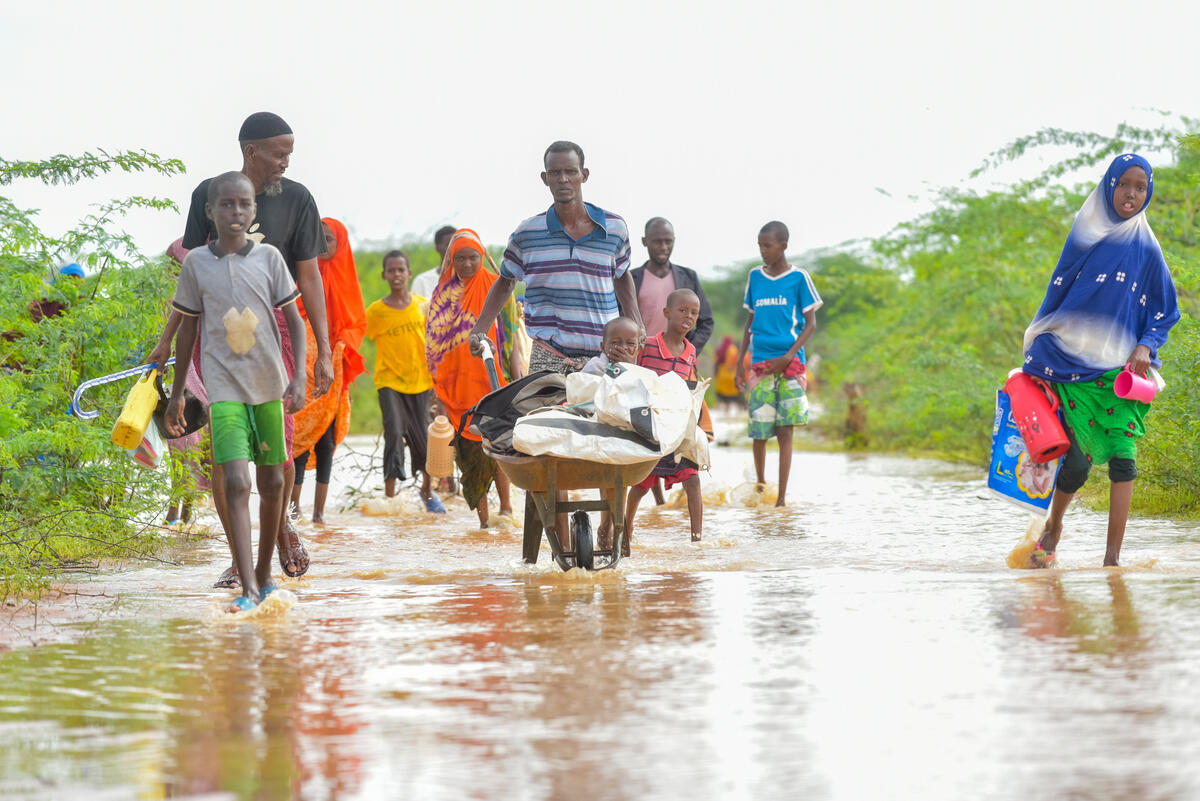 A man pushes a handcart containing a young child and his belongings through floodwaters accompanied by other family members.