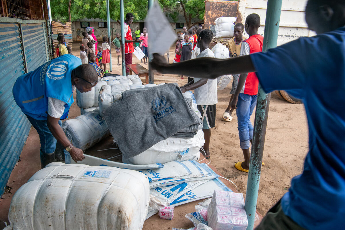 A UNHCR staff member hands plastic sheeting and blankets to refugees affected by flooding.