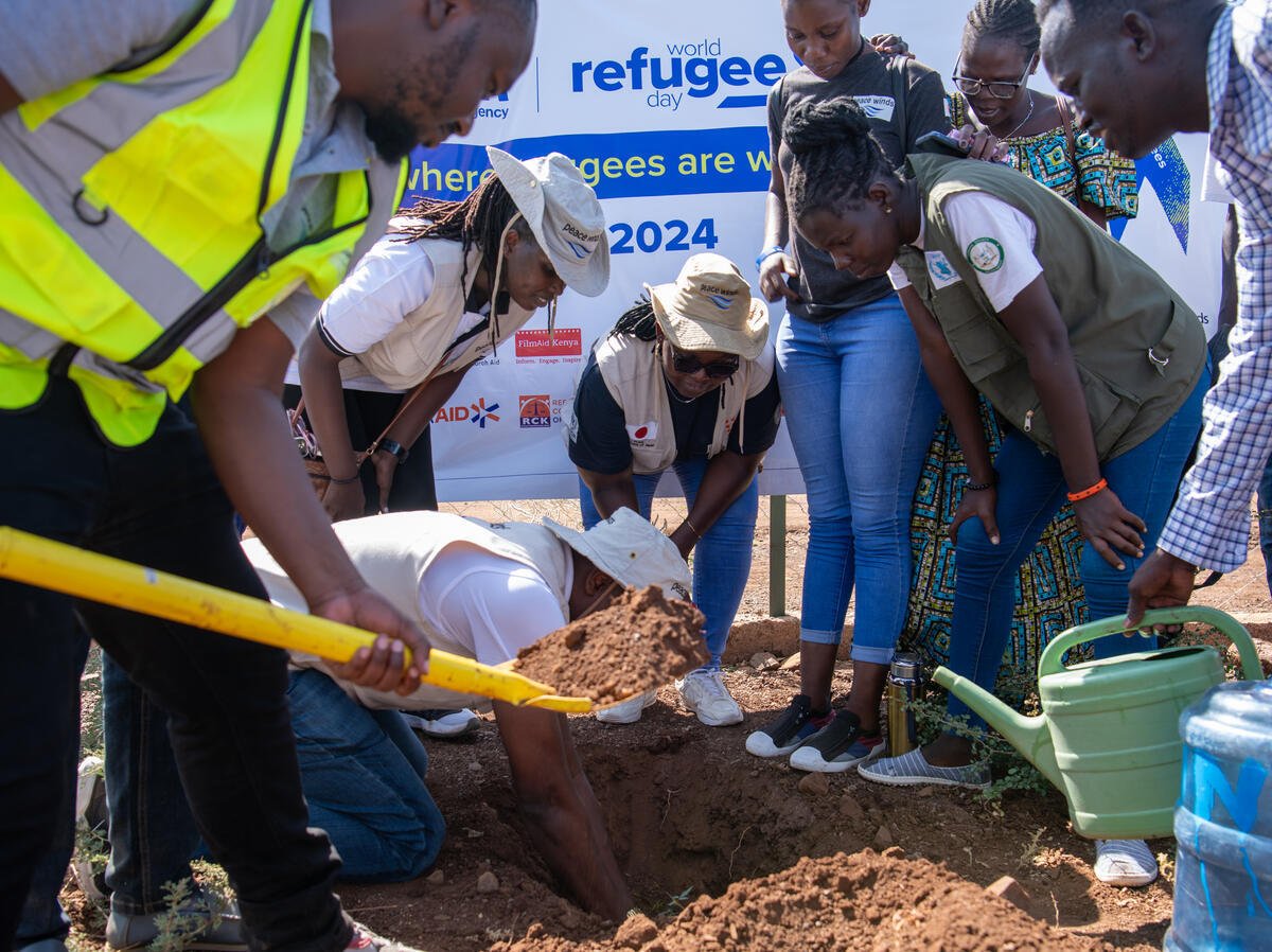 A group of UNHCR partners and refugees work together to dig a hole in the ground.