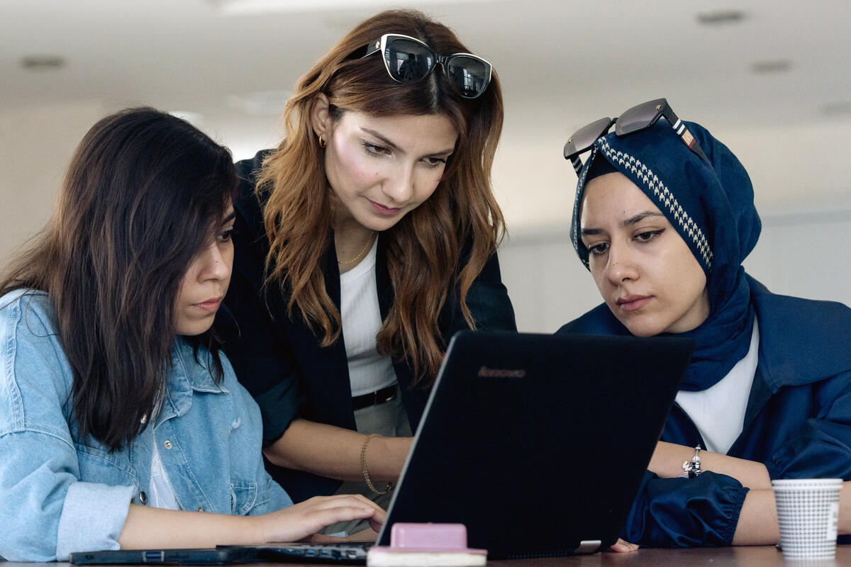 One woman types on a laptop while two other women look at the screen.