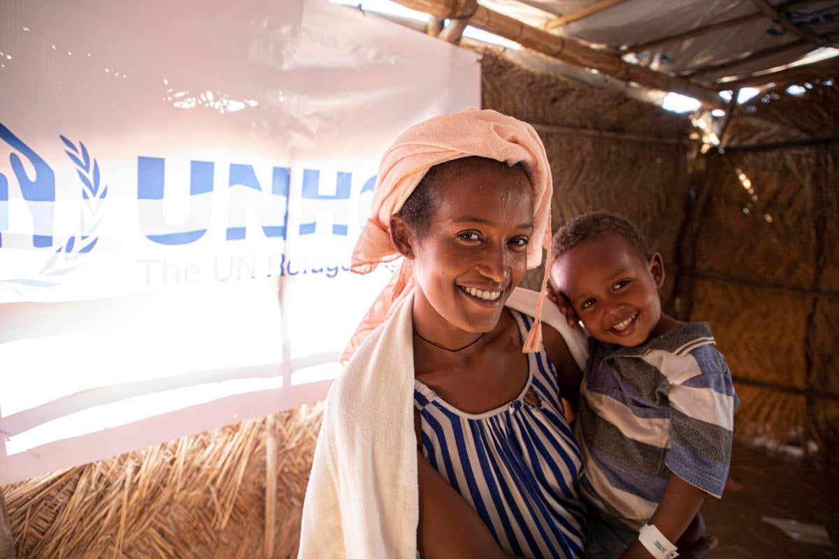 A mother holds her young son inside a UNHCR shelter. Both smile for the camera.