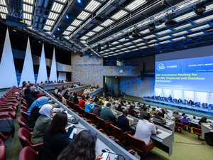 Les participants à l'immense amphithéâtre du Forum mondial sur les réfugiés 2023 regardent une diapositive indiquant &quot;GRF Orientation Meeting for Forcibly Displaced and Stateless Participants&quot; (Réunion d'orientation du GRF pour les participants déplacés de force et apatrides).