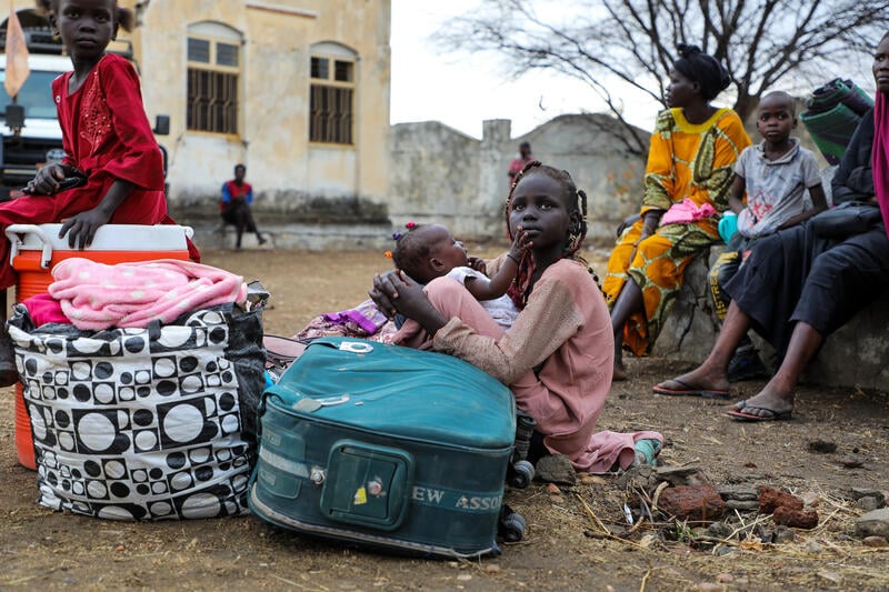A girl holds a baby surrounded by her family and their luggage at a transit point near the South Sudanese border.