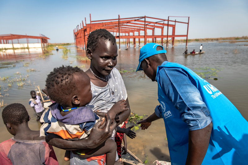 A man in a UNHCR vest help a mother and her children out of a canoe.