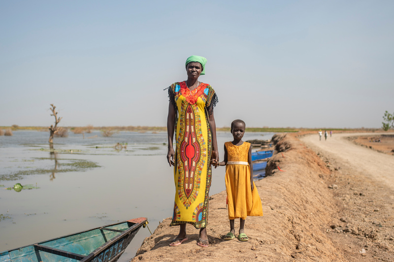 A woman stands on a dike holding a young girl's hand.