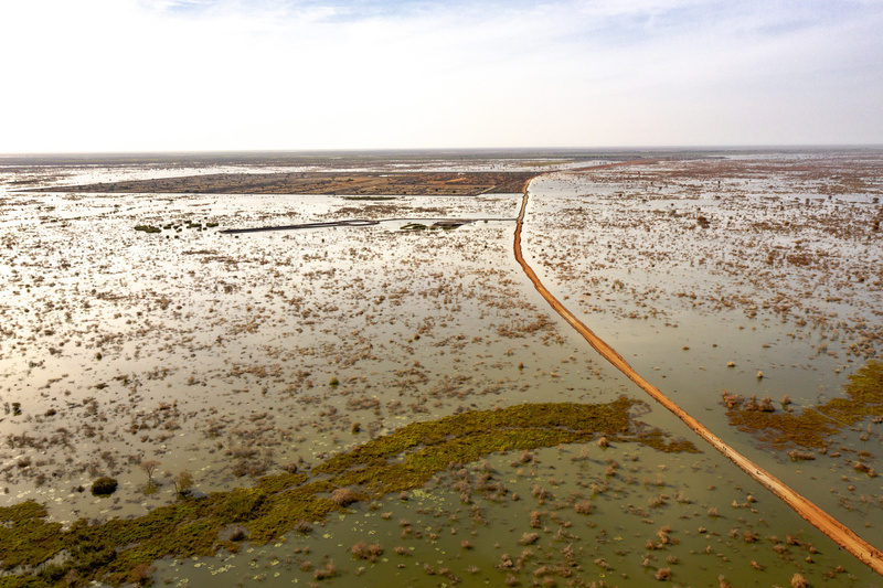 A single road, surrounded by flood waters, leads to a distant camp.