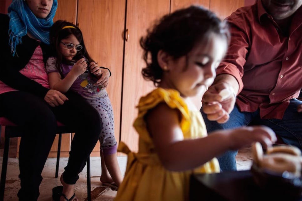 Alberto gives a biscuit to his youngest daughter. In the background are his wife and second daughter