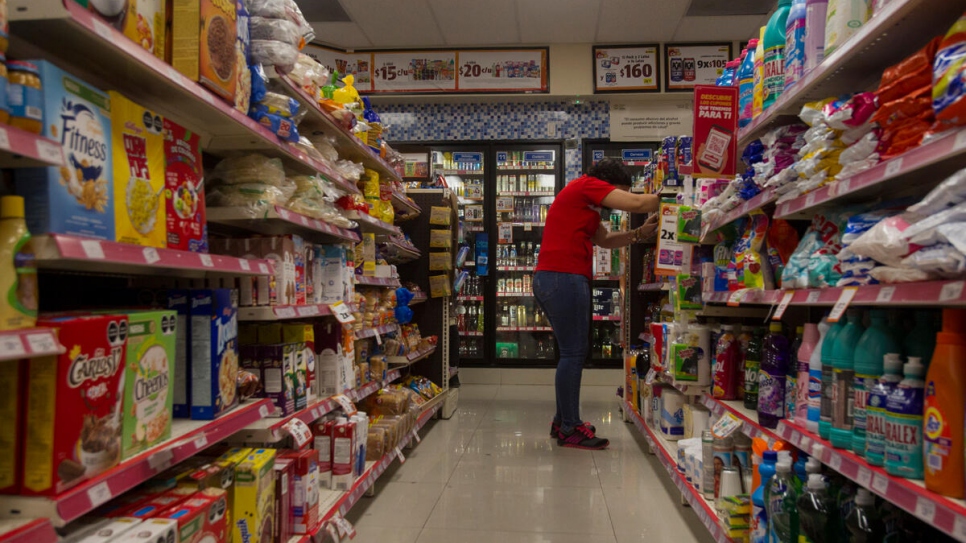 Una refugiada salvadoreña apila estantes en una tienda de conveniencia en Monterrey, México, donde trabaja como supervisora ​​de turno.