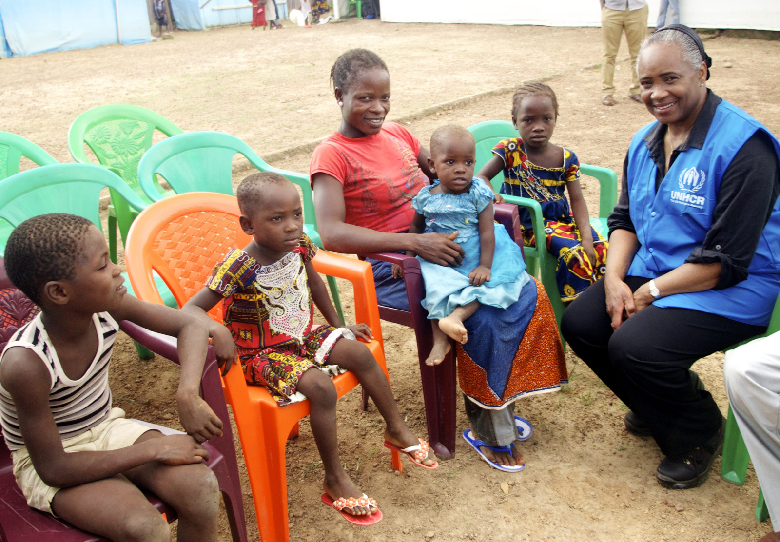 Barbara Hendricks talks to a mother and children, sitting on plastic chairs.